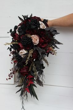 a bridal bouquet with red and black flowers is held by a woman's hand