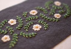 embroidered fabric with white flowers and green leaves on grey background, closeup shot from eye level