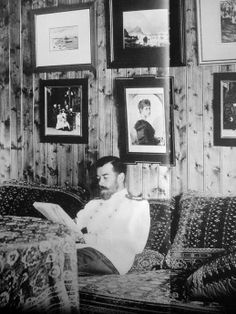 a man sitting on top of a couch next to a wall covered in framed pictures