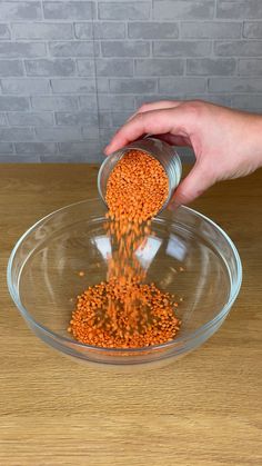 a person scooping red lentils into a glass bowl on a wooden countertop