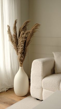 a white vase with some dry grass in it sitting on the floor next to a couch