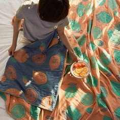 a woman sitting on top of a bed next to a plate of fruit and an orange