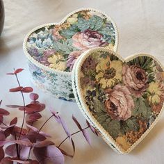 two decorative heart shaped boxes sitting on top of a table next to flowers and a vase