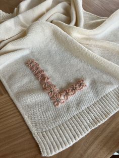 a white sweater with pink flowers on it sitting on a wooden floor next to a table