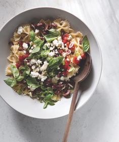 a white bowl filled with pasta salad and topped with fettuccine, tomatoes, olives, and spinach