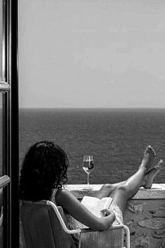 a woman sitting on top of a chair next to a window with a glass of wine