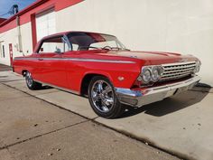 an old red car parked in front of a building