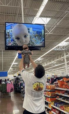 a man is holding up a baby in front of a television with an alien head on it