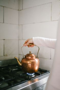 a person is holding a tea kettle on top of the stove and touching it with their hand