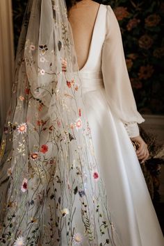 the back of a bride's wedding dress with flowers on it and veil over her head