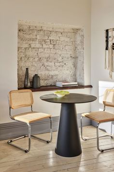 a table with two chairs around it in front of a brick wall and wooden floor