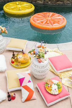 an outdoor table with pillows, plates and vases on it next to a swimming pool