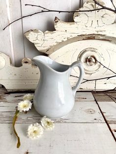 a white vase sitting on top of a wooden table next to some branches and flowers