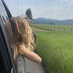 a woman is looking out the window of a car on a road with grass in front of her