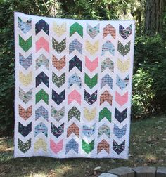a colorful chevroned quilt hanging on a clothes line in front of some trees