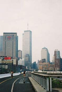 two people walking down the road in front of tall buildings