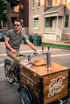 a man riding on the back of a bike next to a small cart filled with coffee