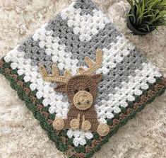 a crocheted blanket with a moose on it and a potted plant in the corner