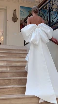 a woman in a white dress walking down some stairs with her back to the camera