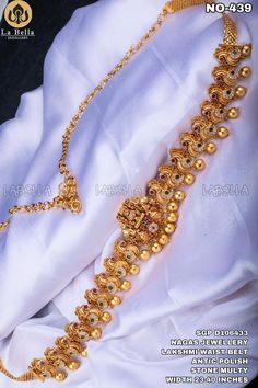 the gold necklace is being displayed in front of a white cloth with beads on it