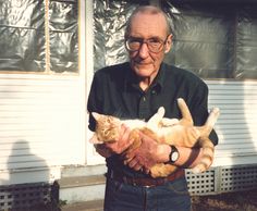 an old man holding two cats in his hands