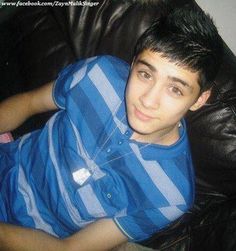 a young man sitting on top of a black leather couch wearing a blue shirt and looking at the camera