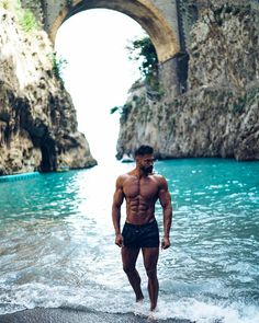 a shirtless man standing in the water next to a stone bridge over a river