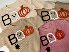 three baby sweaters with pumpkins and ghost faces on them, all in different colors