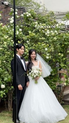 a bride and groom posing for a photo in front of some bushes with white flowers