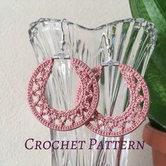 pink crochet hoop earrings on clear vase next to potted plant and white wall