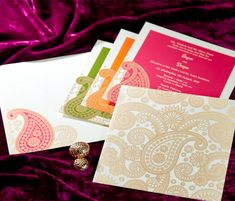 wedding cards with paisley designs on them and a gold broochy pin sitting next to it