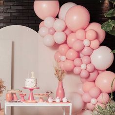 a table topped with lots of balloons and desserts next to a wall covered in greenery