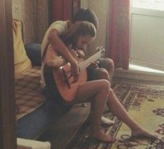 a woman sitting on the floor playing an acoustic guitar