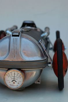 an old model motorcycle with a speedometer on the front and rear wheels, sitting on a white surface