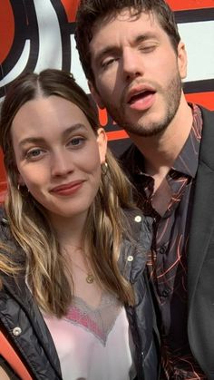 a young man and woman posing for a photo together in front of an orange wall