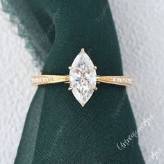 an engagement ring with a pear shaped diamond in the center on top of a green cloth