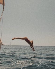 a man dives into the ocean from a sailboat while another person swims in the water