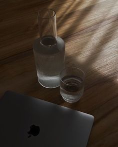 an apple laptop computer sitting on top of a wooden table next to a glass vase