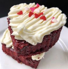 a piece of red velvet cake with white frosting and hearts on top is sitting on a plate