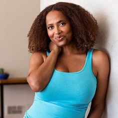 a woman leaning up against a wall with her hand on her chin and looking at the camera