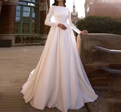 a woman in a white wedding dress standing on a bridge with her hands on her hips