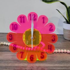 a colorful clock with numbers on it sitting on a table next to a potted plant