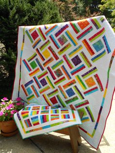 a colorful quilt sitting on top of a wooden bench next to a potted plant