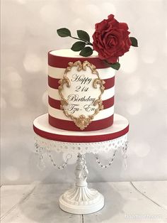 a red and white striped birthday cake with a single rose on top, sitting on a stand