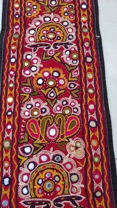 an old red and black cloth with colorful designs on the bottom, sitting on a white surface