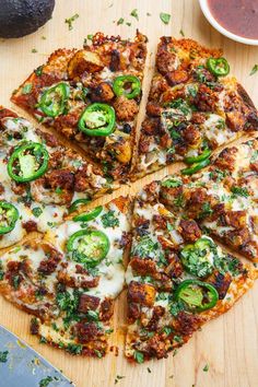 a pizza cut into four slices on top of a wooden cutting board with sauce and green peppers