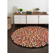 a multicolored round rug on the floor in front of a white brick wall