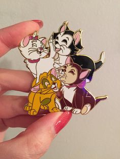a hand holding three disney pin badges in it's left palm, and the other one has a cat on it