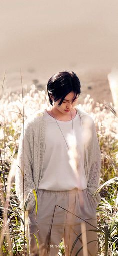 a woman standing in tall grass next to the ocean with her eyes closed and looking down