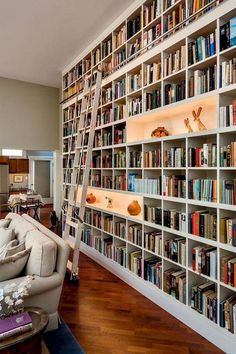 a living room filled with lots of books and furniture next to a wall covered in shelves